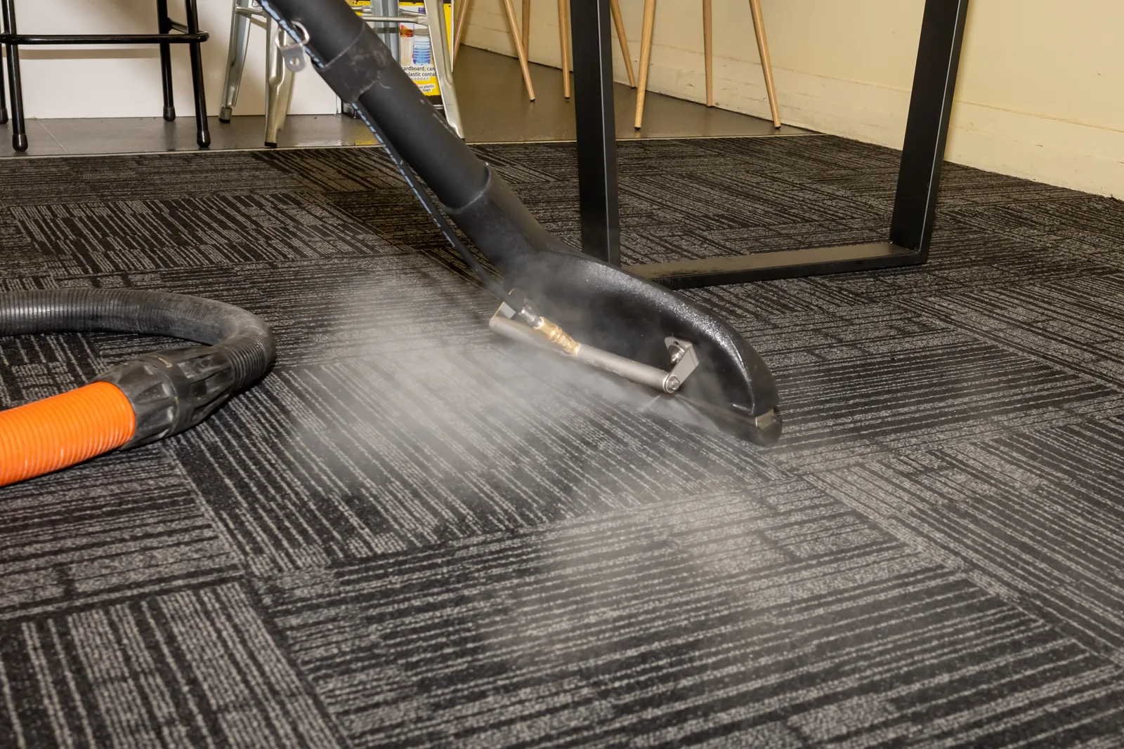 Professional carpet cleaning wand spraying hot water and cleaning solution into carpet during a hot-water extraction pass